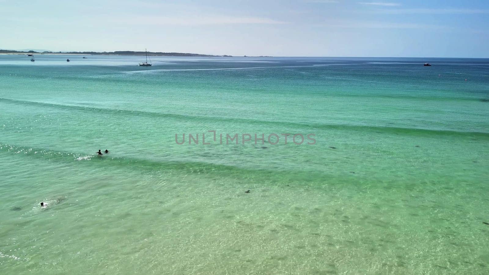 A tranquil beach view highlights the beauty of clear, turquoise waters and people relishing the warm sunlight