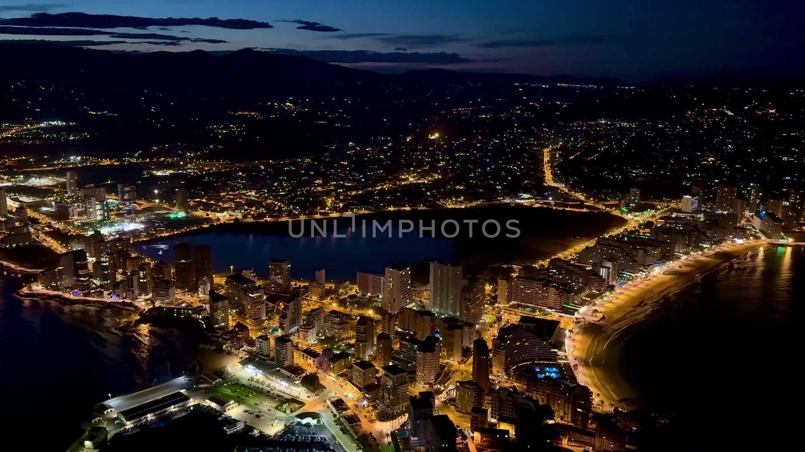 Aerial view of a vibrant coastal city illuminated at night, showcasing beautiful lights and scenery.