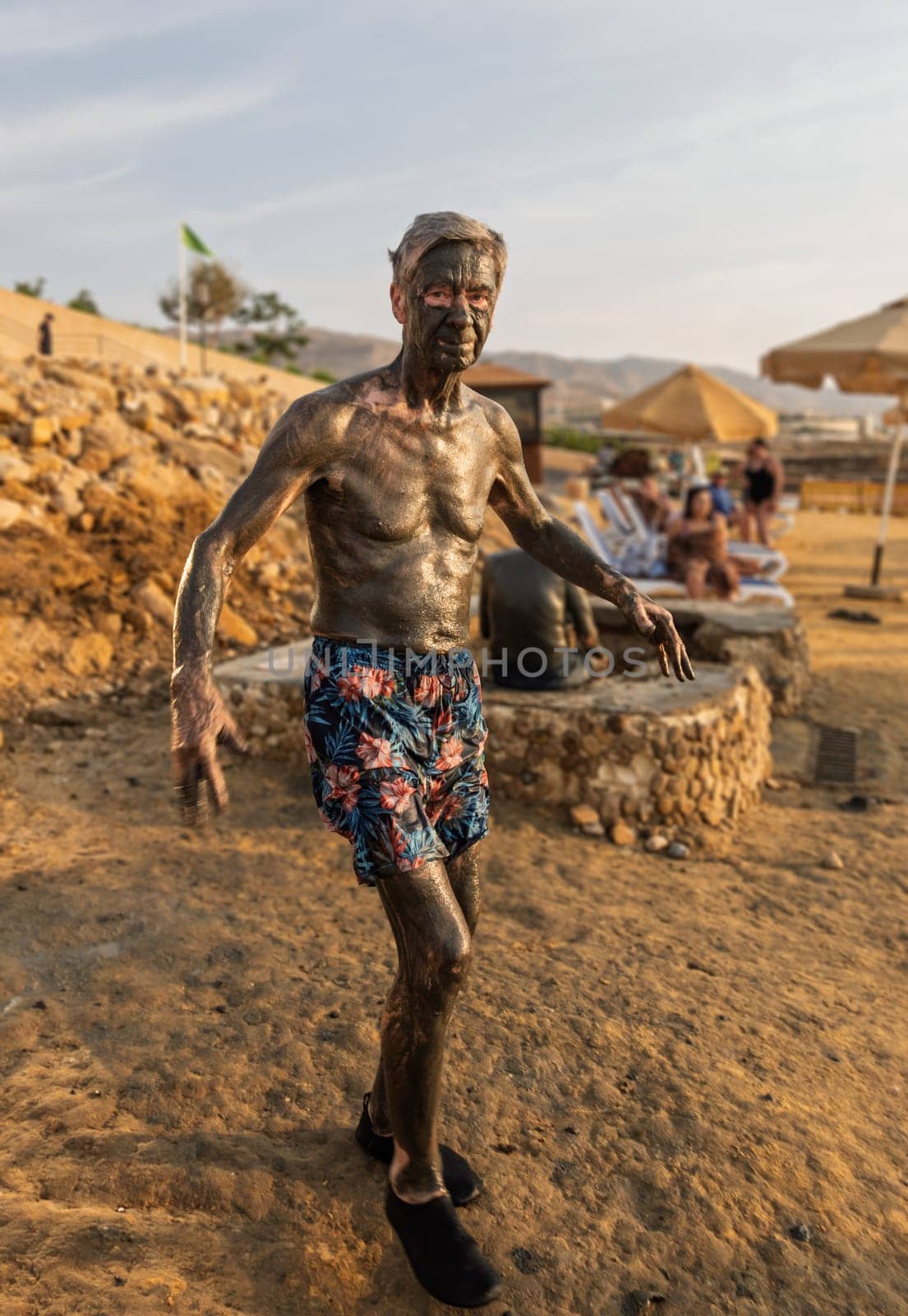 Senior adult man spreading dark mud from the floor of Dead Sea which is said to be good for skin care and wrinkles