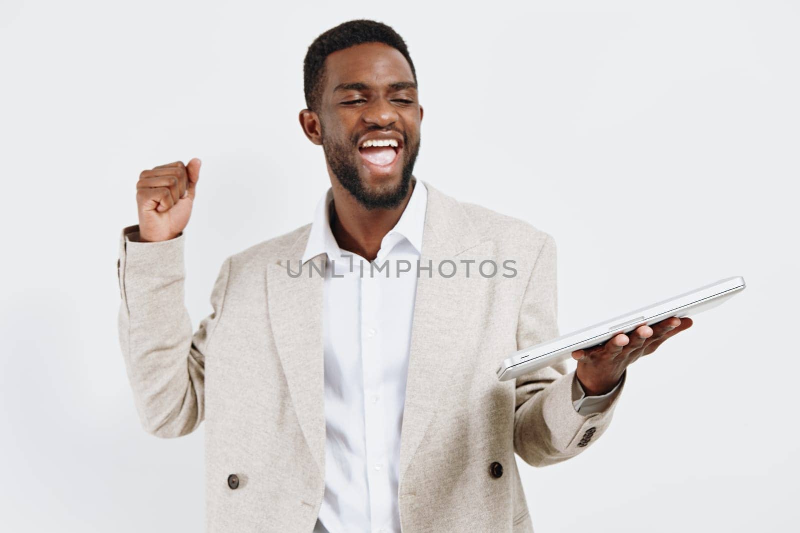 Happy man expressing excitement and success, dressed in smart casual attire, holding tablet device, standing against a blank white backdrop, showing enthusiasm and achievement. Concept: professional achievement and joy.