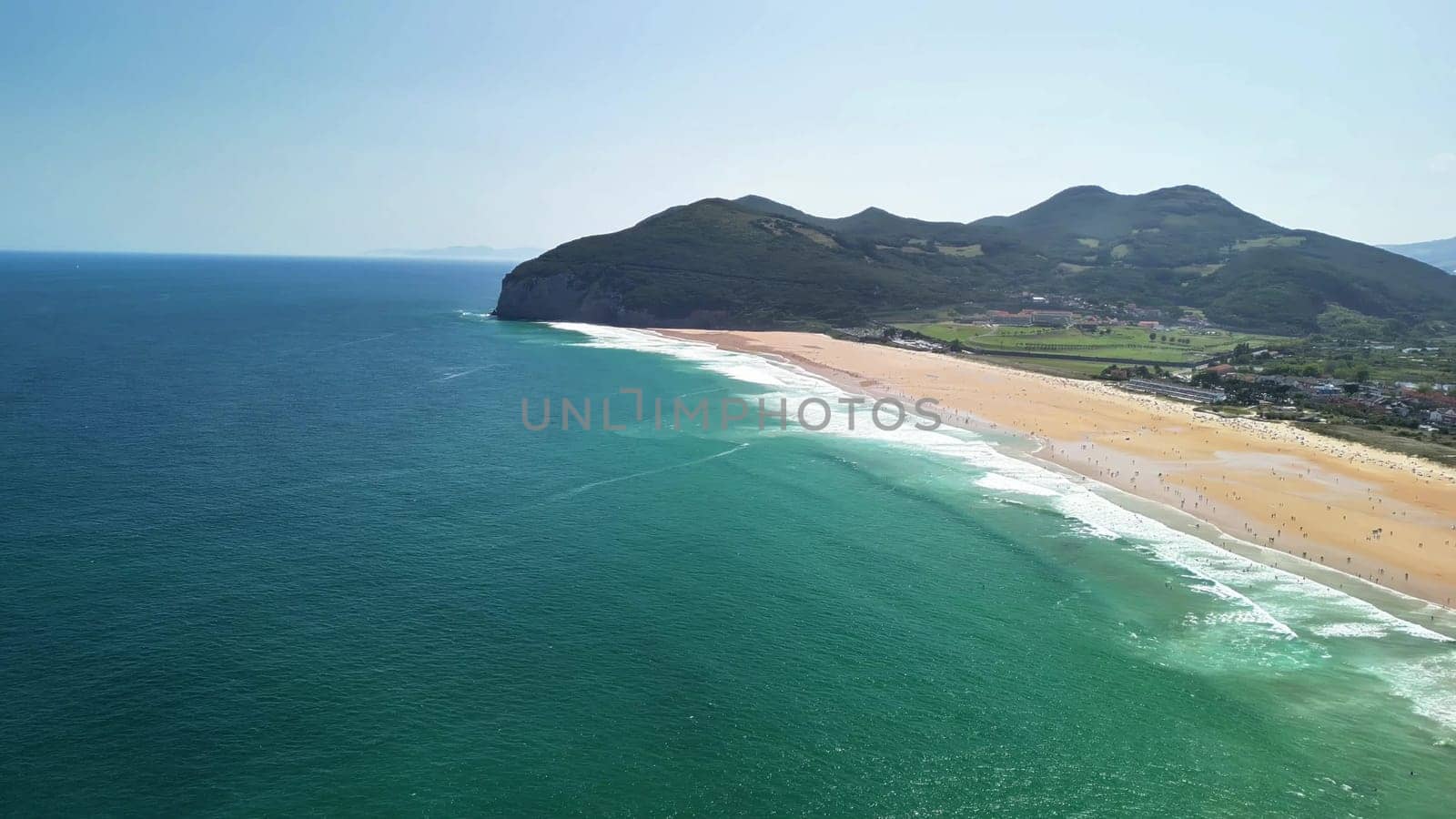 Experience stunning aerial views of a golden beach bordered by majestic mountains and vibrant turquoise waters