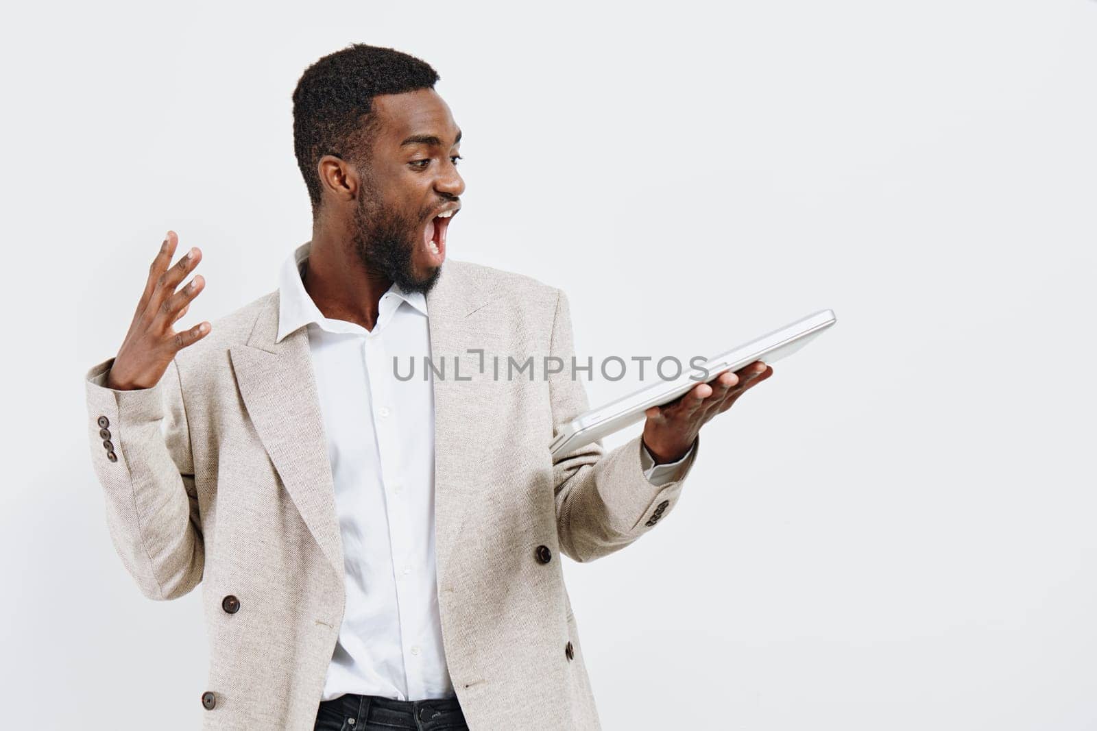 Enthusiastic man in a beige blazer and white shirt holding a tablet, demonstrating surprise or excitement with an open mouth and raised hand, against a white background. Concept: success, technology, excitement, communication skills, business.