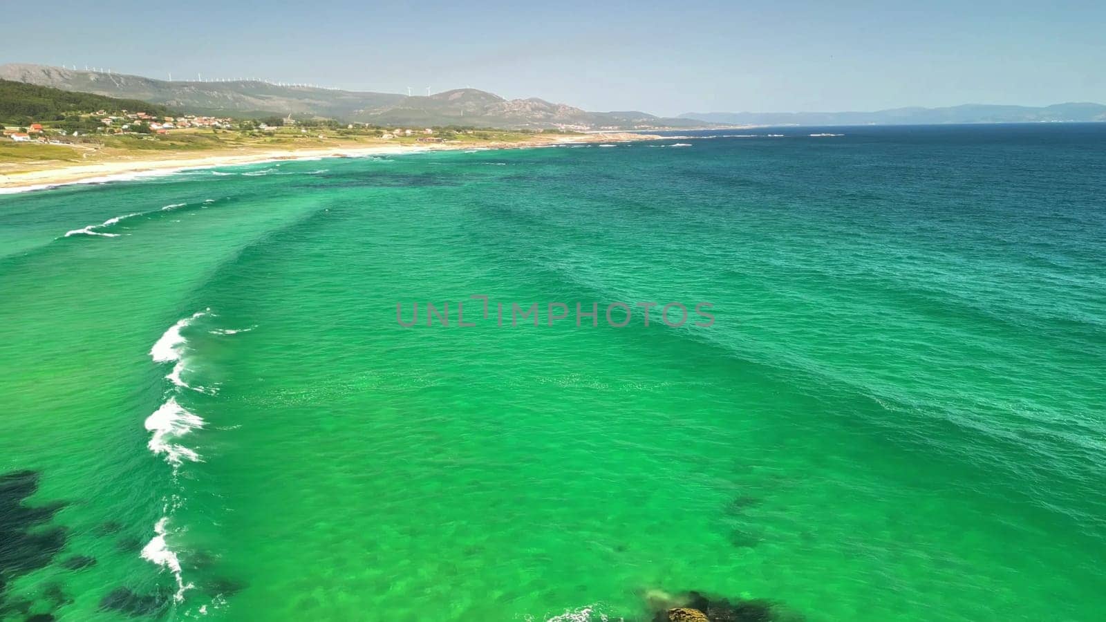 Breathtaking aerial shots showcasing turquoise waves gracefully rolling onto a pristine sandy beach under a clear sky