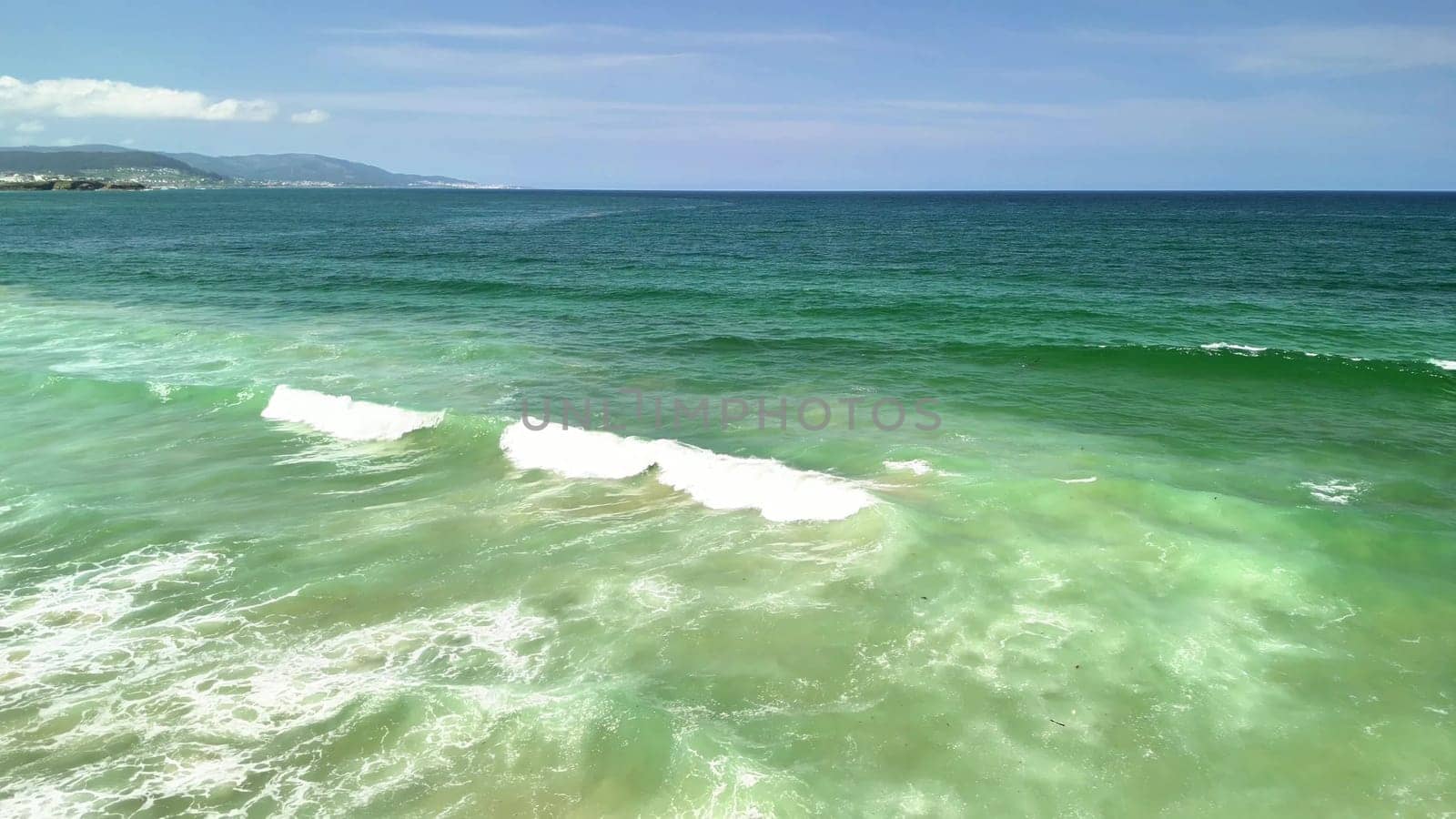 This captivating and stunning aerial seascape stunningly showcases vibrant ocean waves crashing against the sandy shore