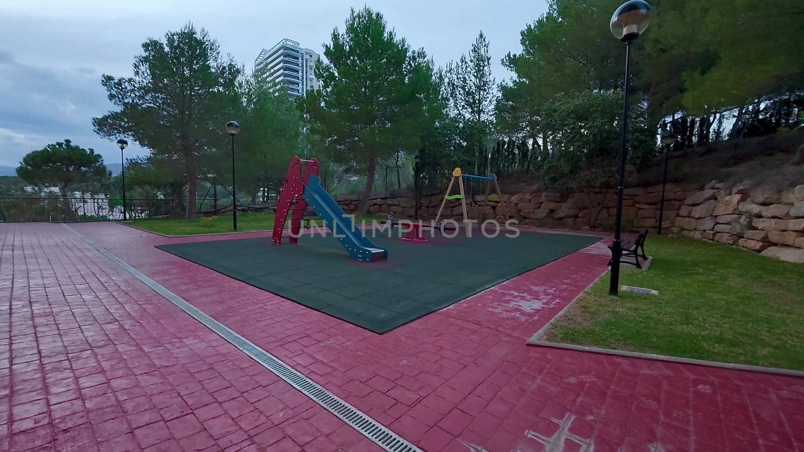 A colorful playground featuring a long slide and several swings is located within a serene park environment
