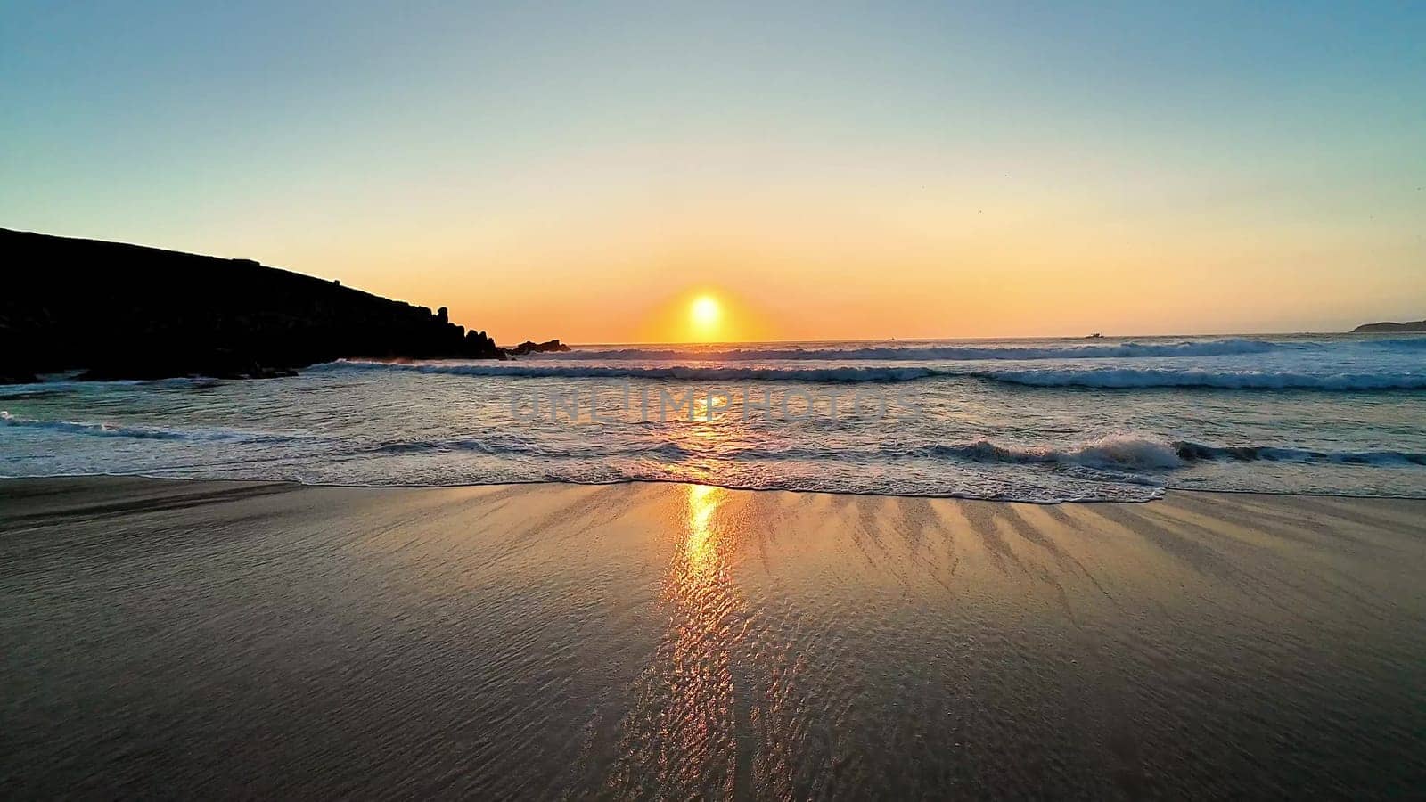 A breathtaking view of the sunset reflecting beautifully on the calm, still waters, creating a serene beachscape