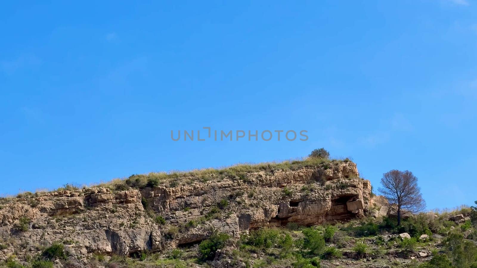 There is a stunning view of a rocky cliff, beautifully adorned with vibrant greenery, all set beneath a clear blue sky