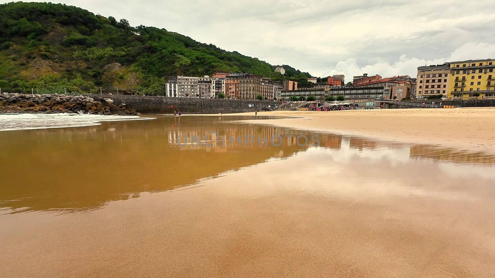 A tranquil beach scene showcasing a picturesque coastal town alongside lush, green hills beneath a cloudy sky
