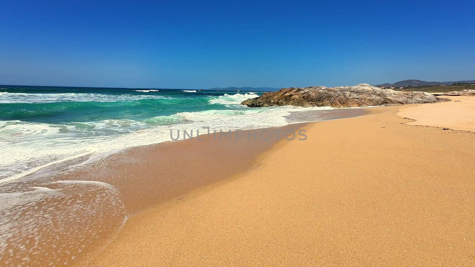 A breathtaking beach landscape showcasing golden sand alongside lively waves beneath a clear, vibrant blue sky