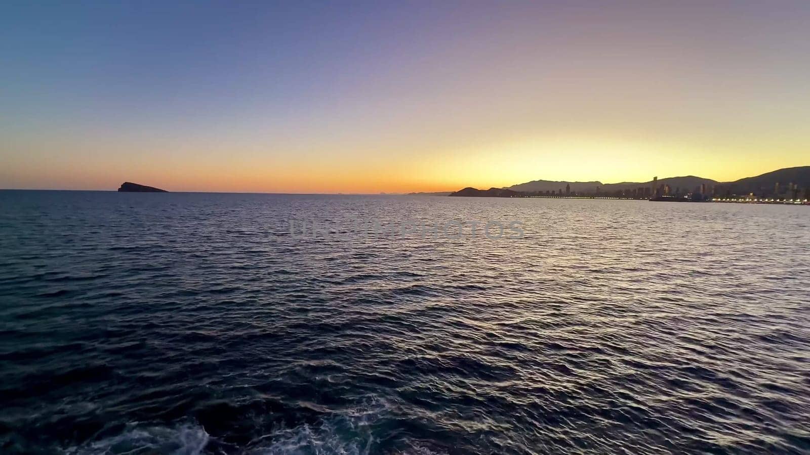 A beautiful sunset viewed over the calm ocean waters, showcasing vibrant colors and a scenic coastline.