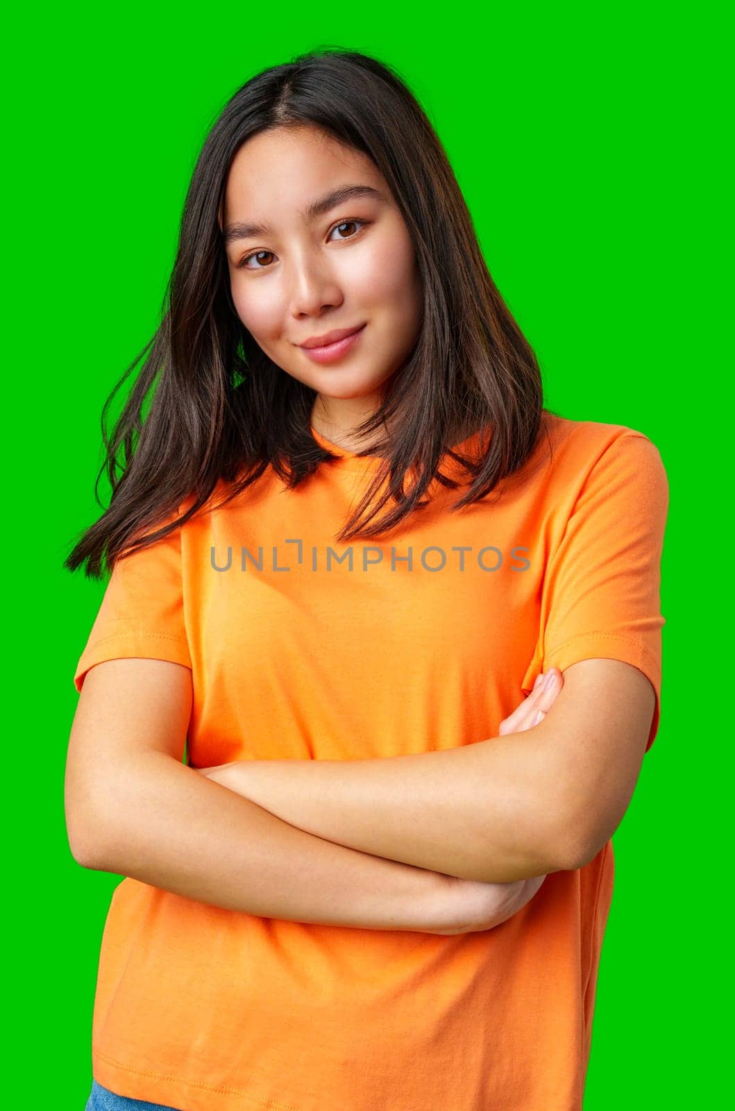 A young woman with straight, dark hair stands confidently with her arms crossed, wearing an orange shirt. The vibrant green background adds energy to the composition.