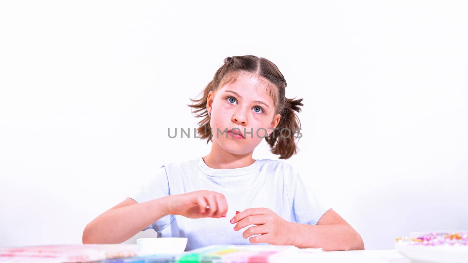 Delicate fingers of a young girl navigate through a treasure trove of bright, multicolored beads, each compartment revealing a new hue to choose from. Shes immersed in the joyful task of stringing together a handmade bracelet, with golden beads and pearls lying nearby to add a touch of sparkle to her creation.