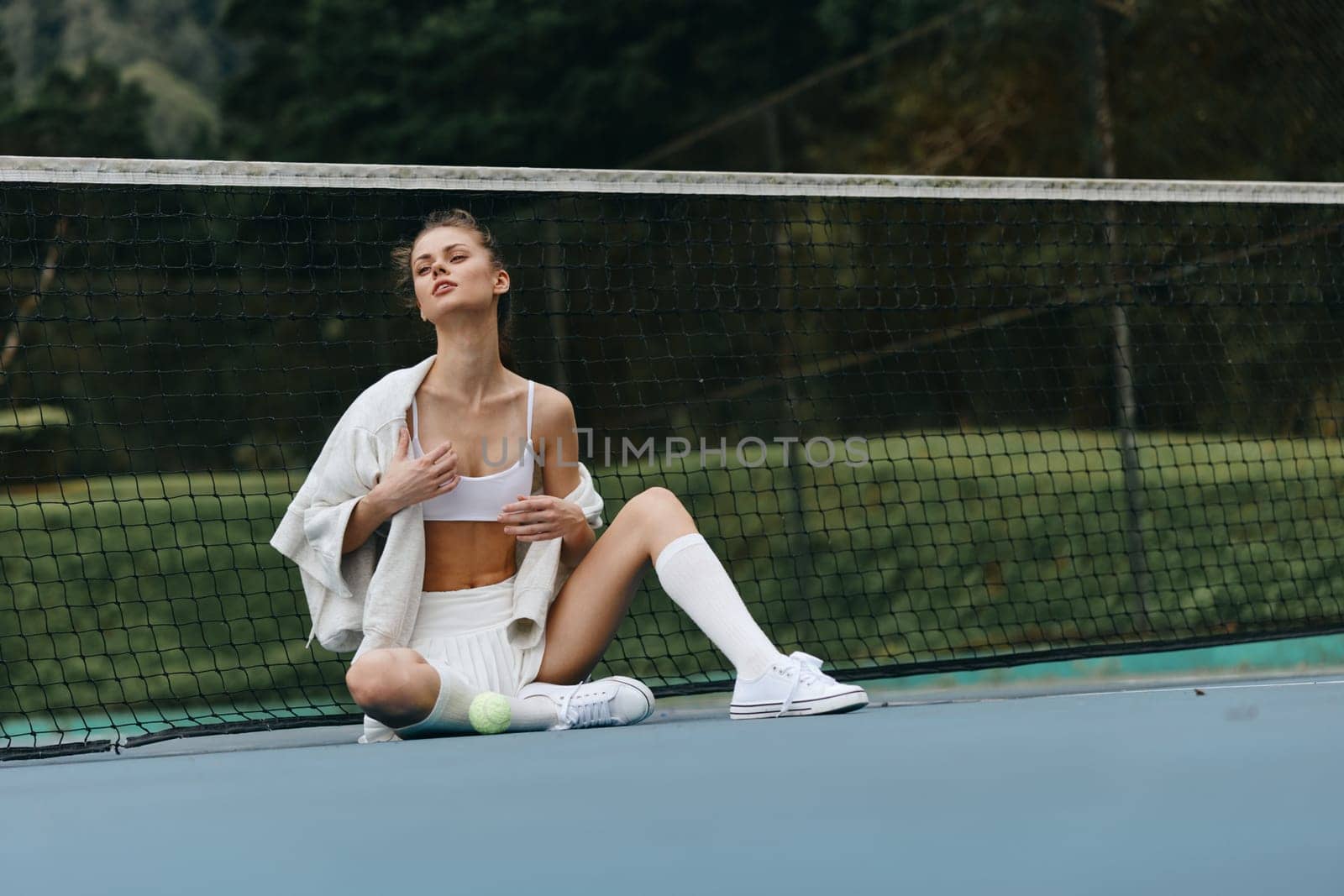 Young athletic woman in sportswear shows emotion while seated on a tennis court, vibrant green surroundings enhance the sporty vibe, ideal for fitness or wellness themes