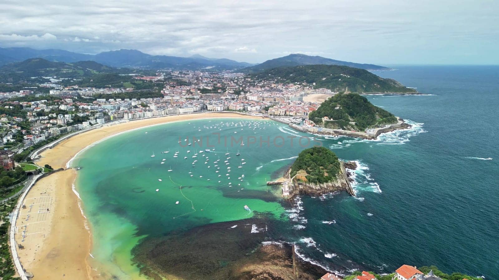 An impressive aerial shot beautifully captures the stunning green waters, sandy beach, and picturesque coastal town
