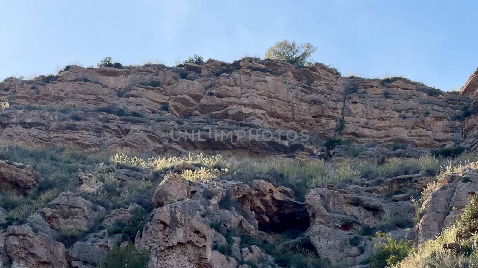A stunning scenic rocky cliffside is beautifully adorned with vibrant lush vegetation and a prominent cave opening