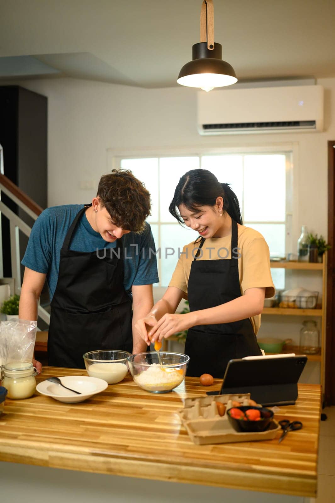 Smiling couple cracking eggs into a bowl while preparing pancake batter in a kitchen.