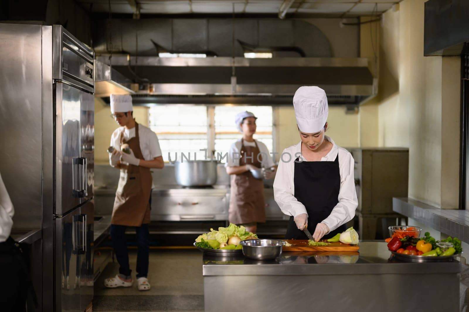 Busy cooking class in session with multiple students in uniforms preparing fresh ingredients.