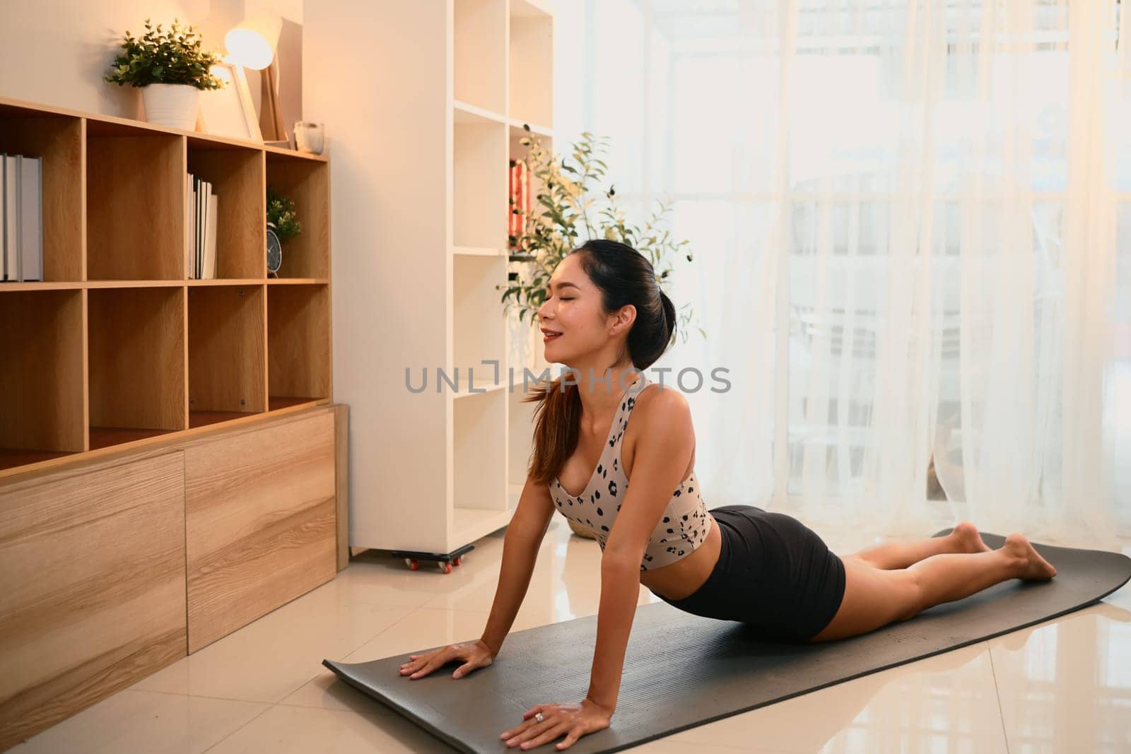 Fit woman doing cobra pose on exercise mat during a home yoga session.