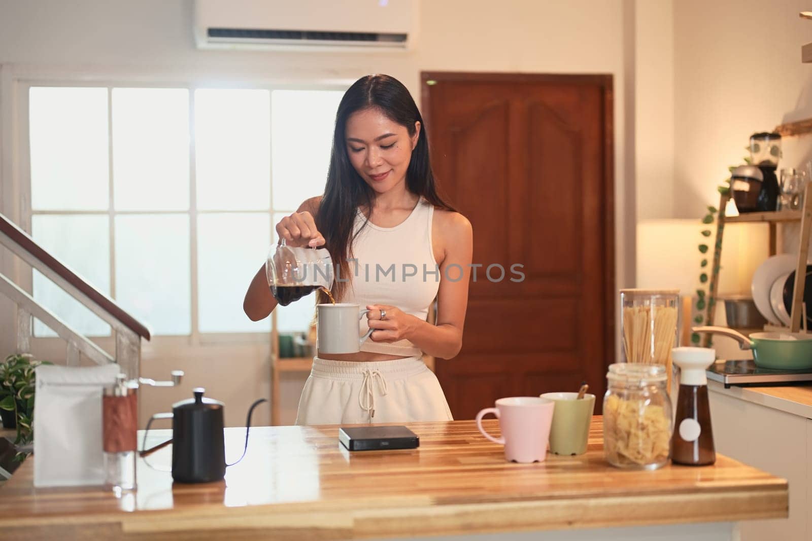 Charming Asian woman preparing her daily cup of coffee in a relaxed kitchen.