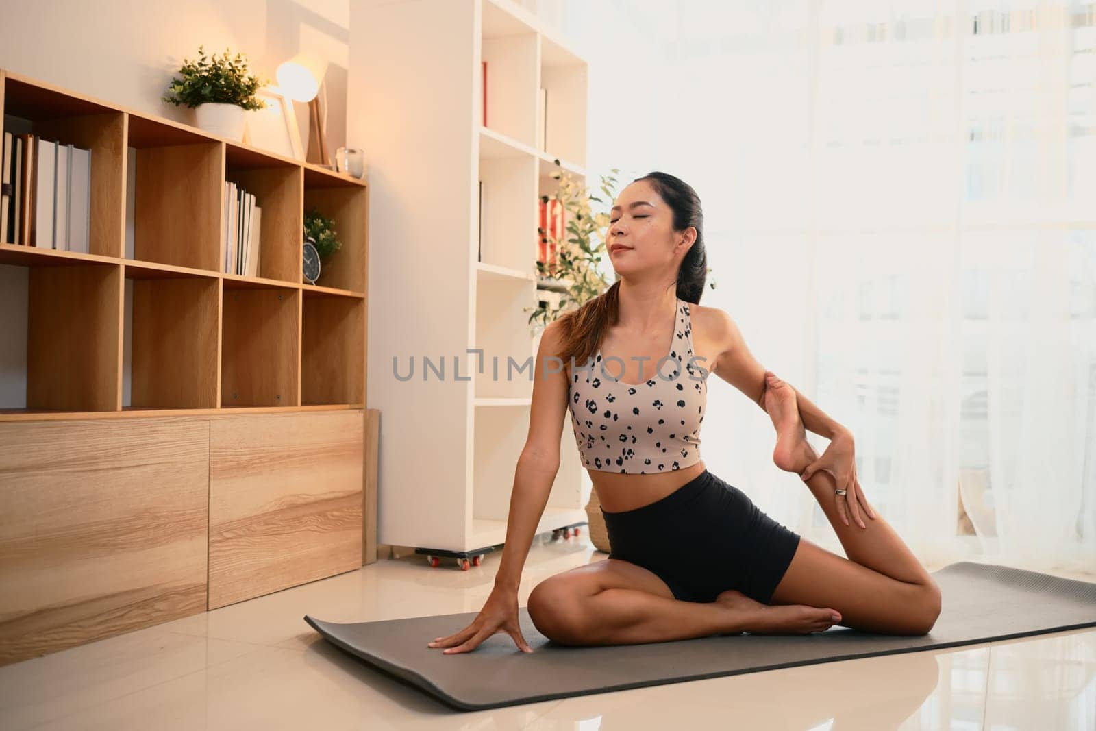 Young woman in activewear practicing yoga on mat in a bright living room.