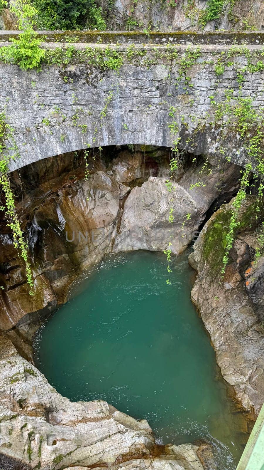 Natural pool in Italian Orrido di Bellano near lake Como surrounded by rocky cliffs and lush greenery beneath a stone bridge, featuring tranquil water and a vibrant nature scene
