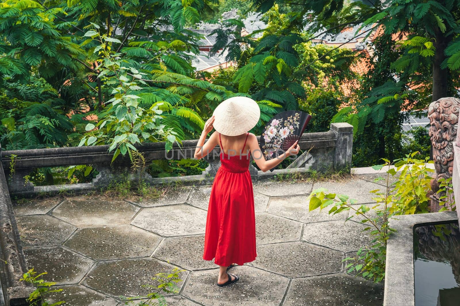 back of beautiful woman tourist traveler in a Vietnamese non la hat with a fan in a garden in Vietnam. Tourism and travel in Asia