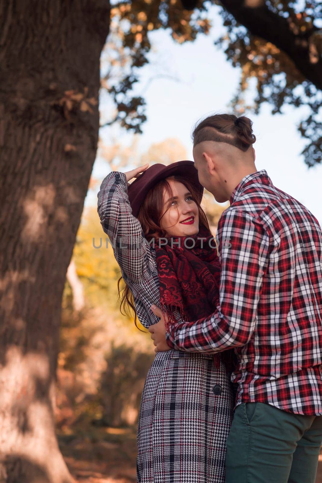 young couple in love walking and having fun in autumn park. they look at each other and hug, against the background of autumn trees. the girl is wearing a dark red hat. concept of romance