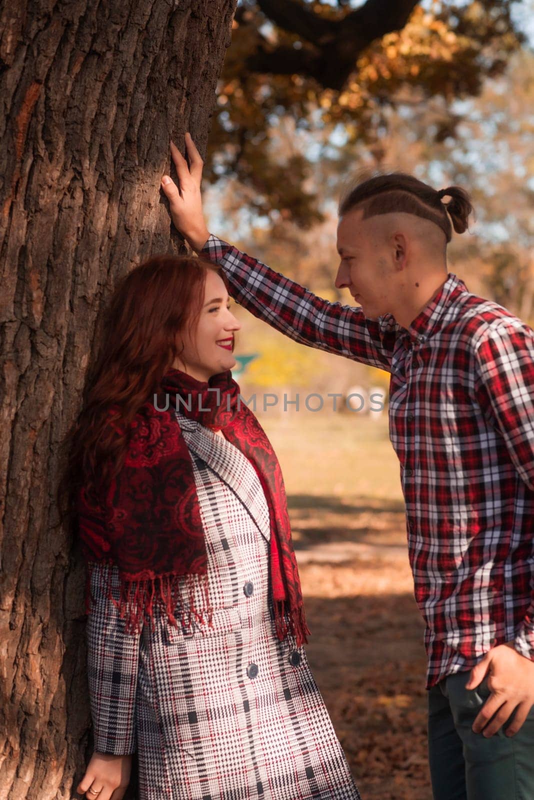 young couple in love hugging in autumn park. they look at each other lovingly. girl in coat, against the background of autumn trees, golden autumn around