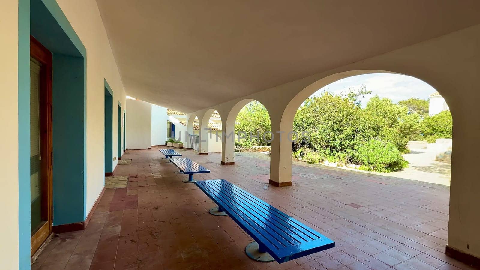 This outdoor corridor offers a serene escape with blue benches and elegant architecture, surrounded by lush greenery