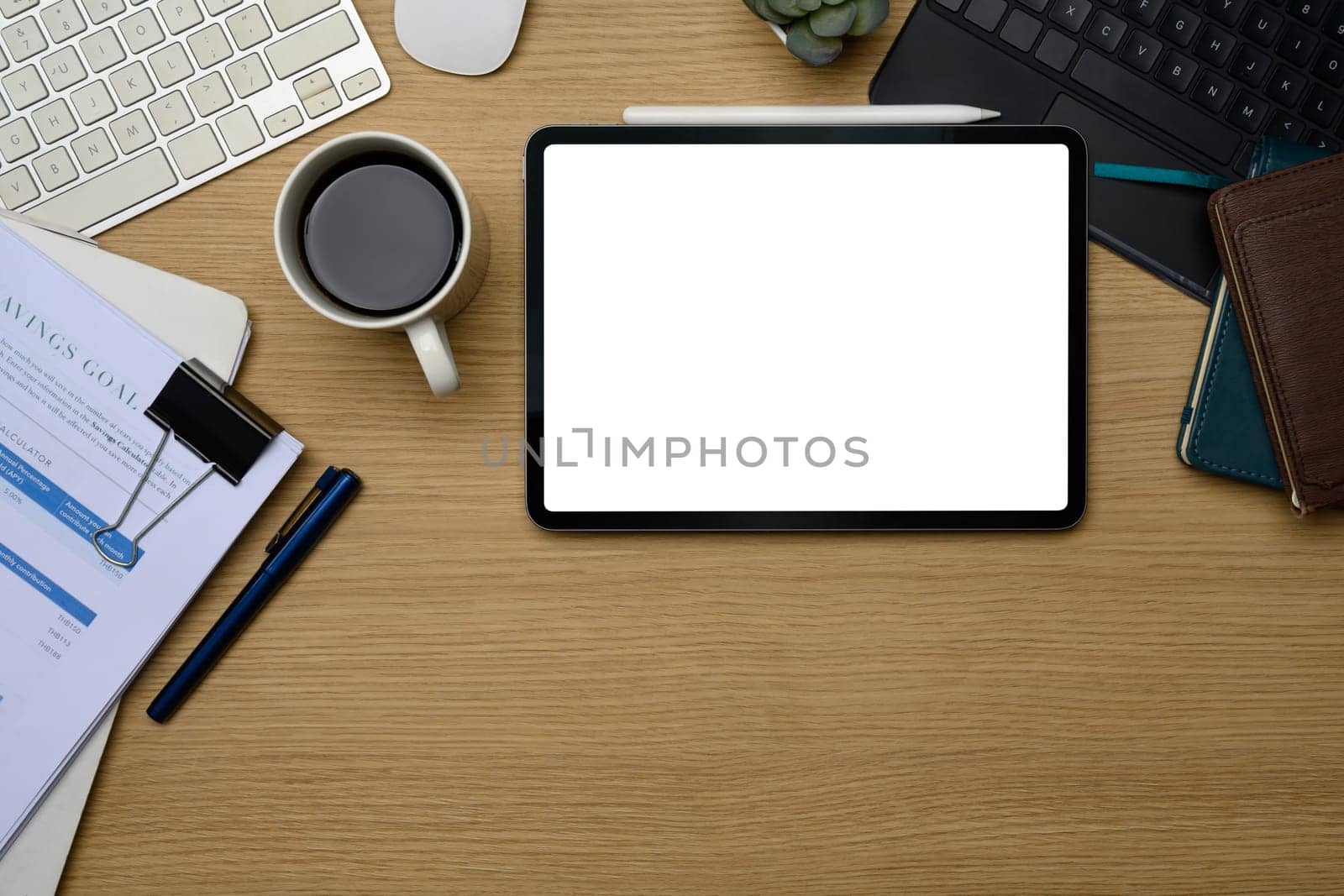 Digital tablet with blank screen on office desk surrounded by coffee, stationery and documents.