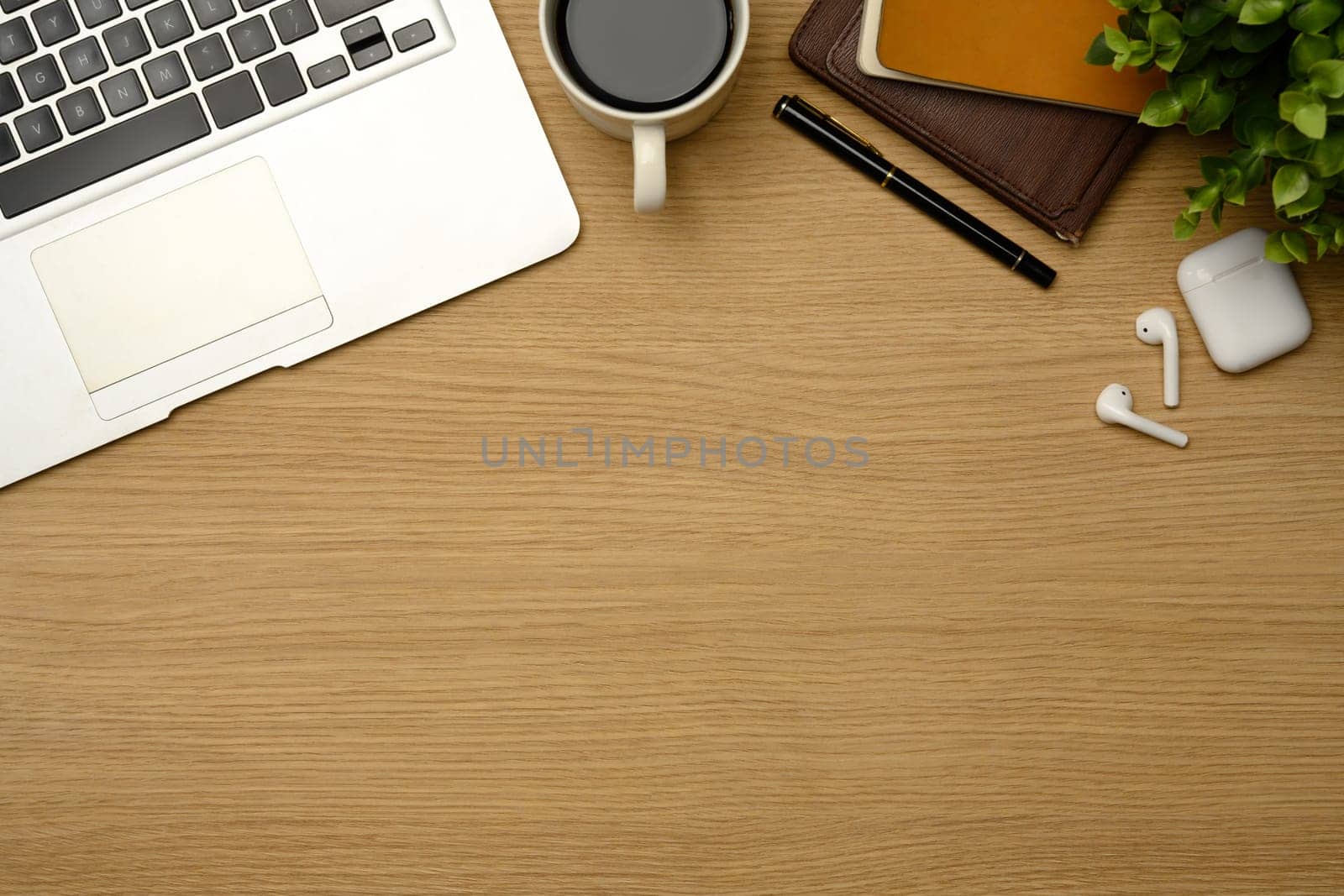 Top view of a wooden desk with laptop, coffee, notebook and wireless earbuds..