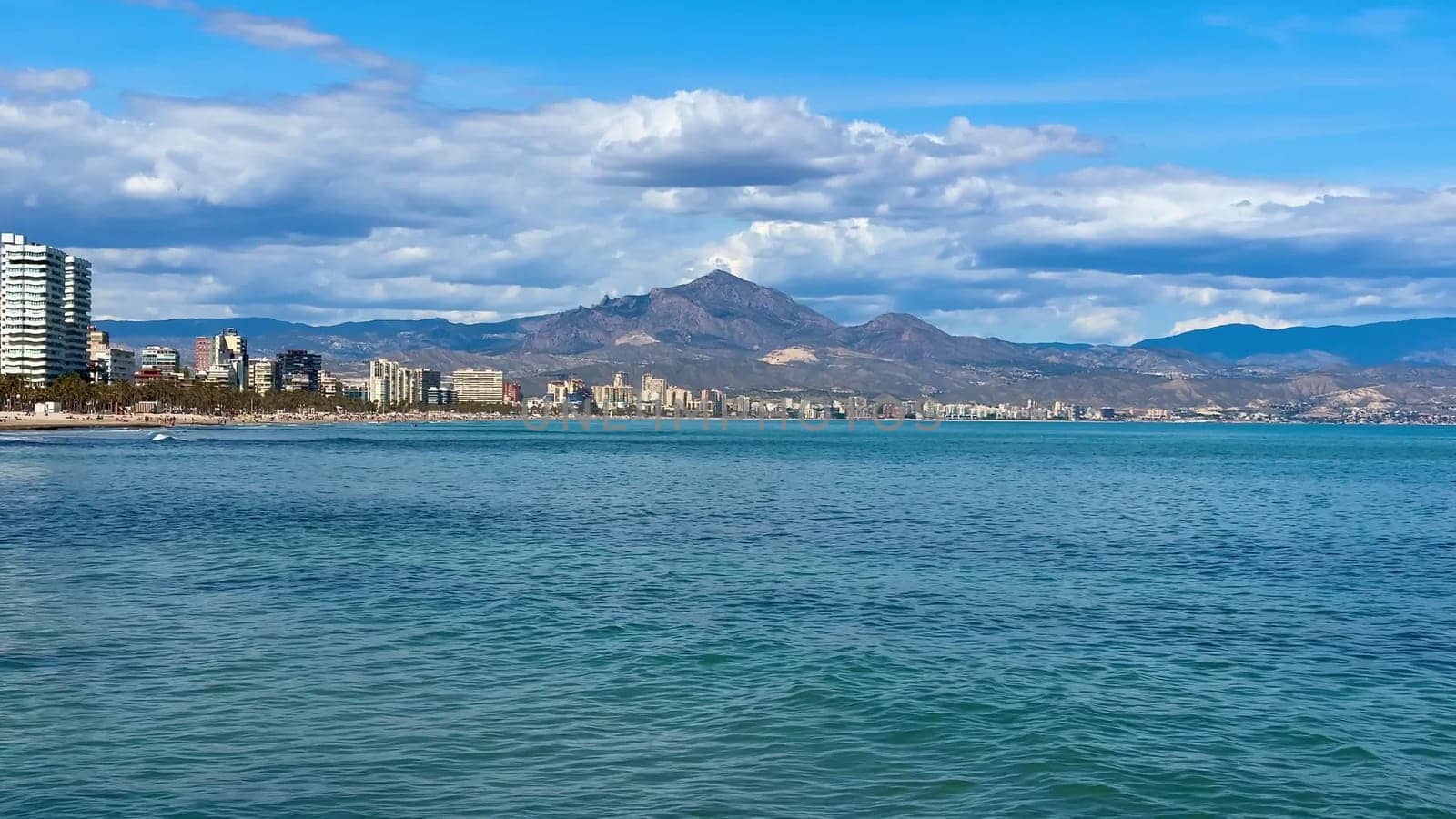 Stunning beach scene beautifully showcasing serene water, majestic mountains, and vibrant blue clouds in the skies