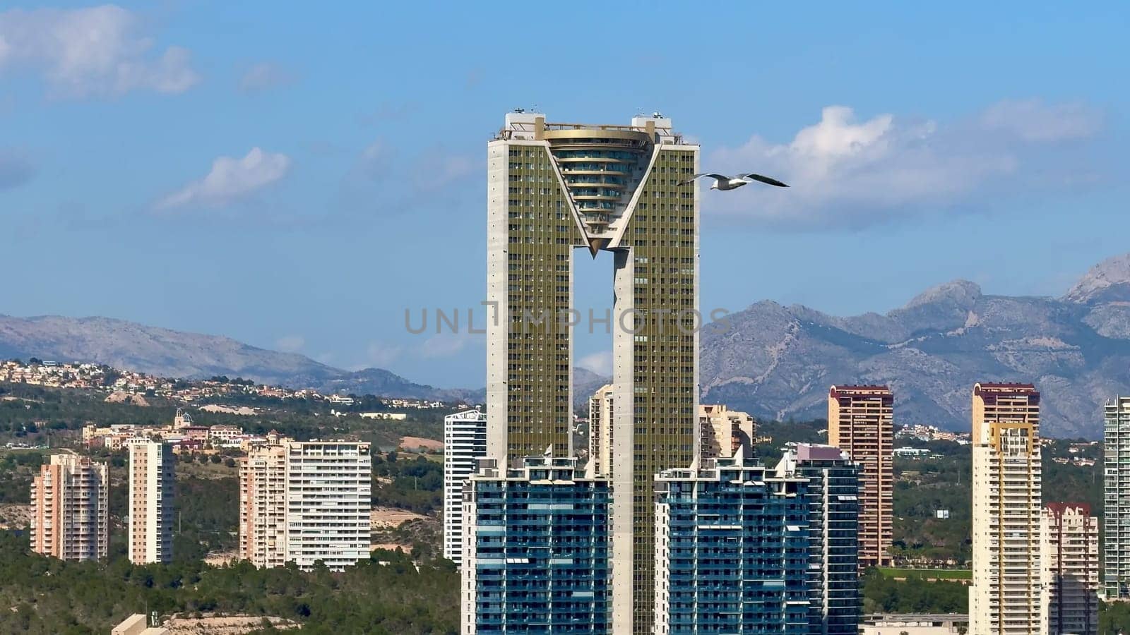 A unique perspective showcasing a modern highrise building within an urban landscape, framed by majestic mountains