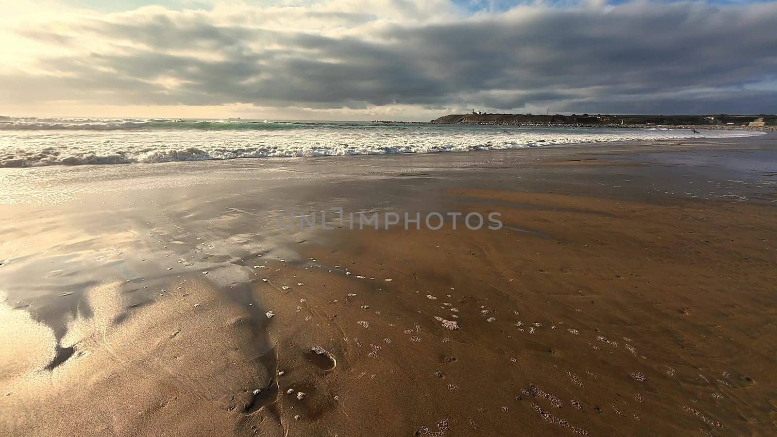 A tranquil beach view displays gentle waves lapping on warm sand beneath a dramatically cloudy sky above
