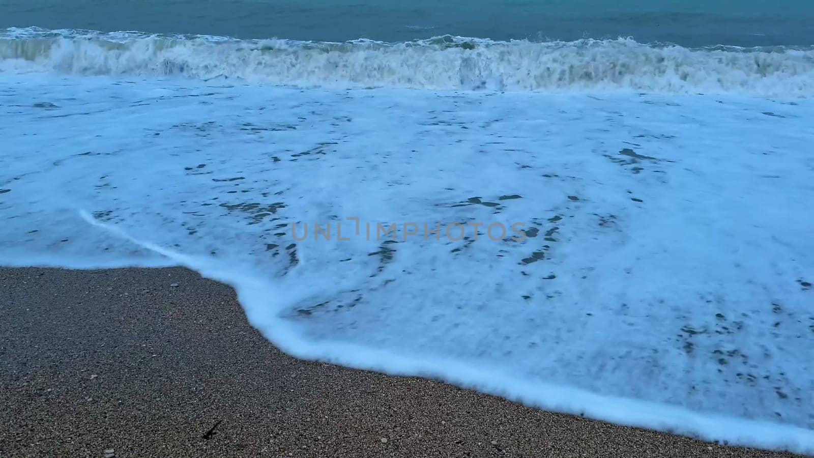 The peaceful ocean waves gently wash over the sandy beach as the sun sets under a beautiful dusk sky