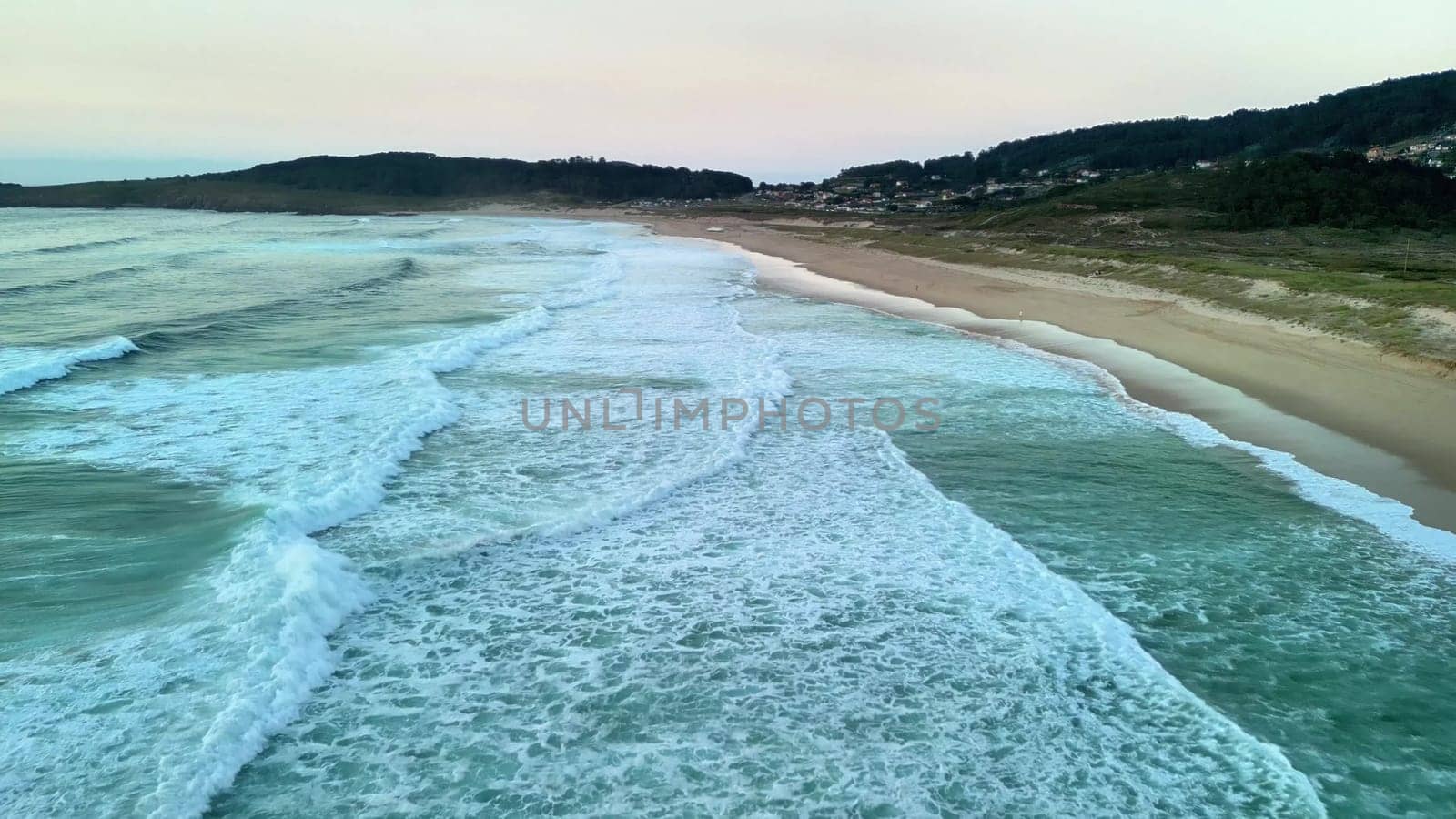 An absolutely stunning aerial view captures the gentle waves rolling smoothly on a tranquil beach at dusk