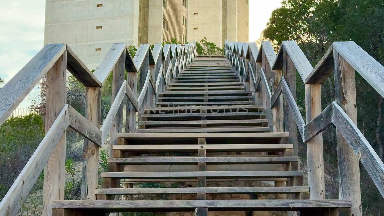 A wooden stairway leads to a modern concrete tower, surrounded by lush greenery that enhances the scenic view