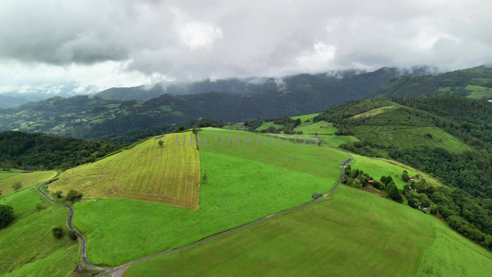 The stunning drone footage beautifully showcases the vibrant green fields and majestic mountains beneath a cloudy sky