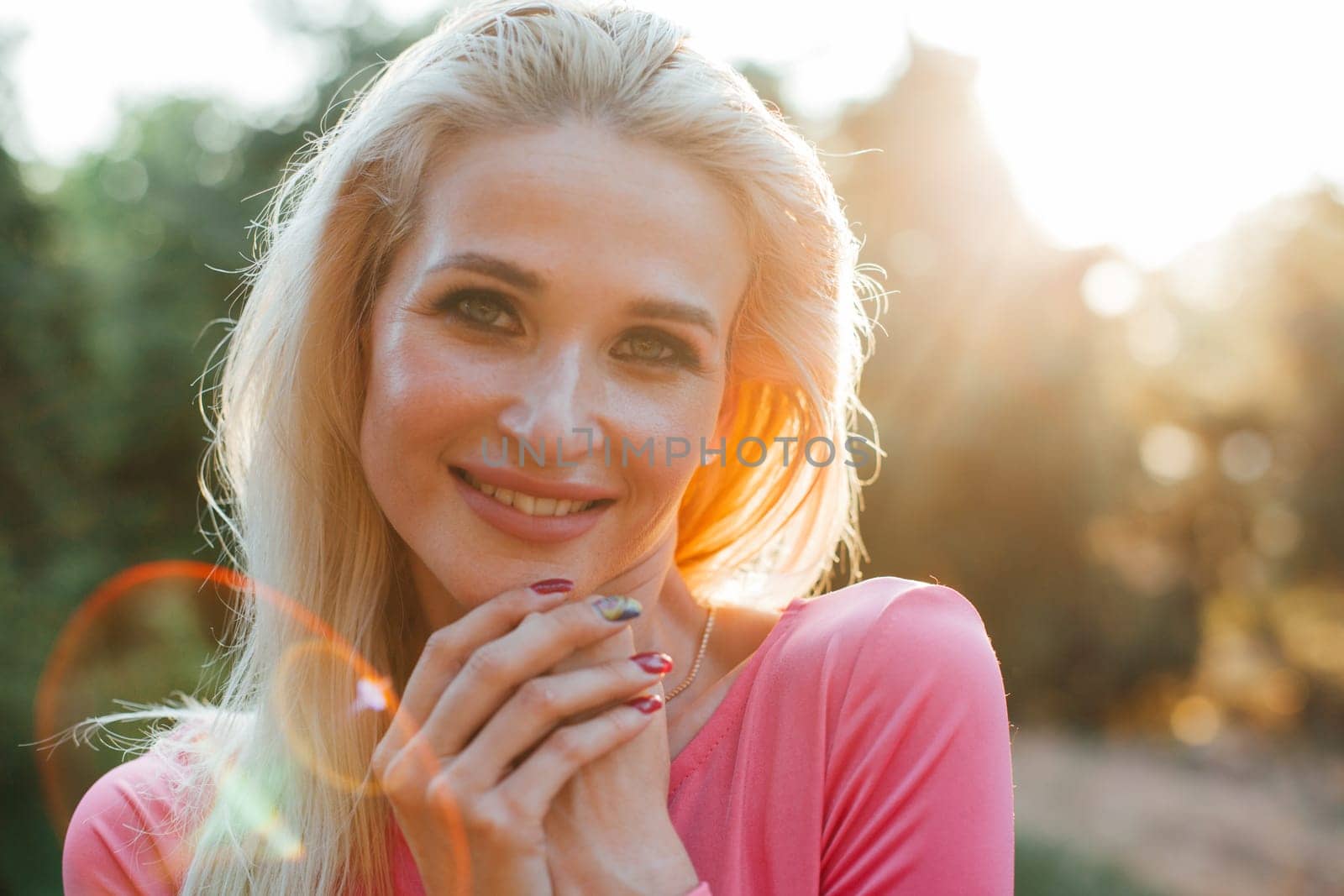 Blonde woman in pink dress smiling at sunset