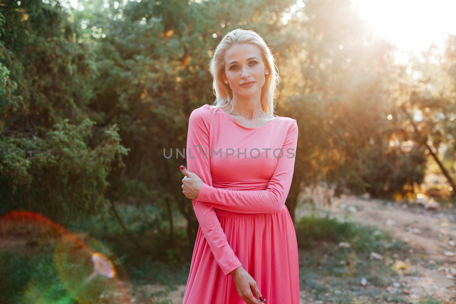 Blonde woman in pink dress smiling at sunset