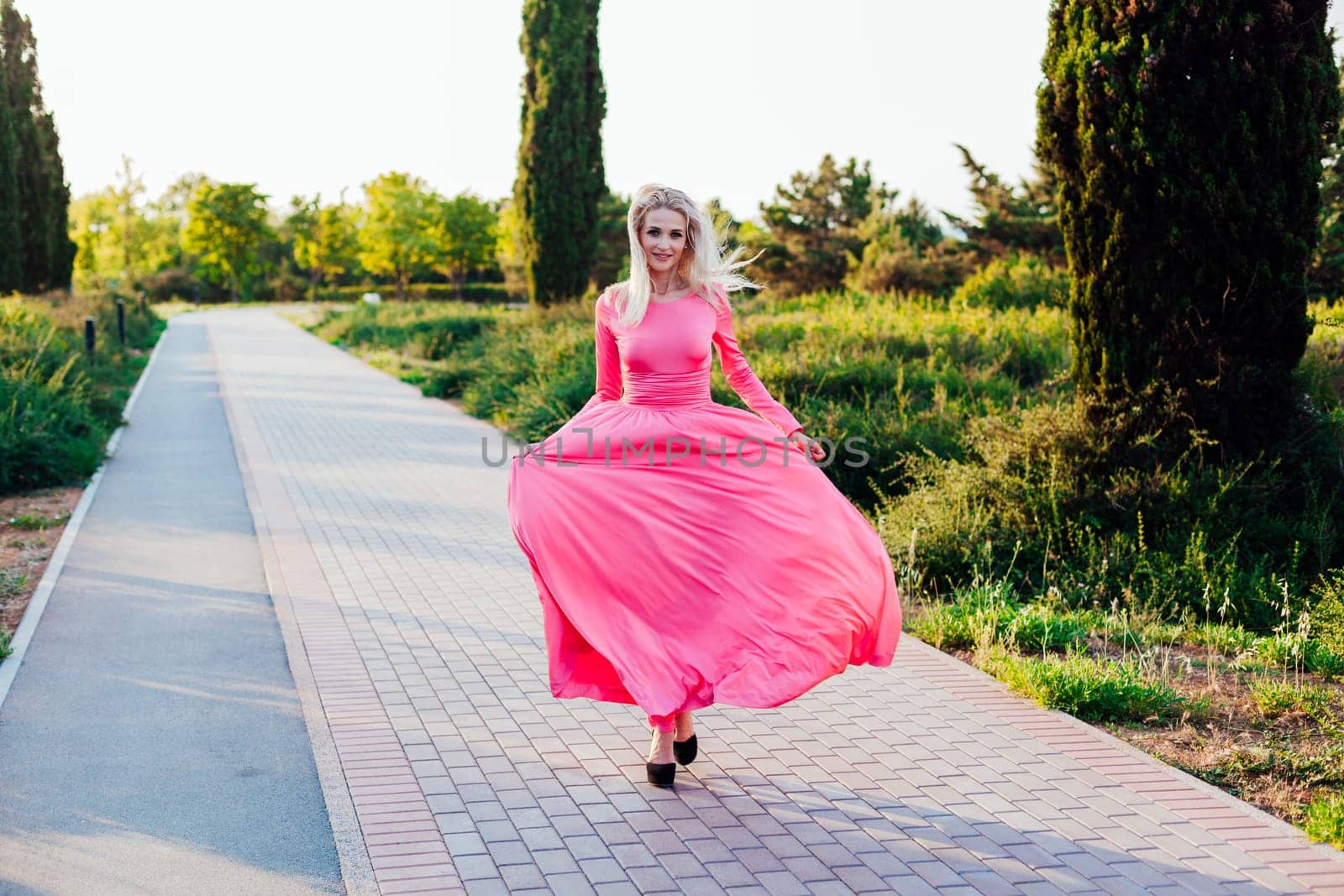 Blonde woman in pink dress walking at sunset in park