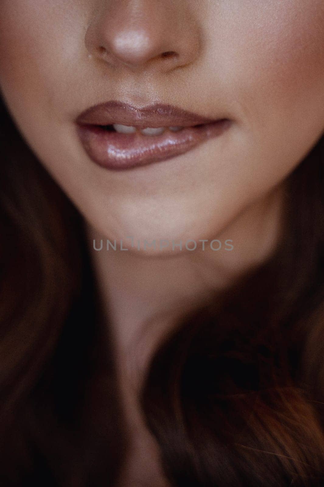 Close-Up of Woman with Glossy Lips and Radiant Skin - Natural Beauty and Minimalistic Makeup Concept, with long dark hair styled in waves. the girl bit her fur coat. High quality photo