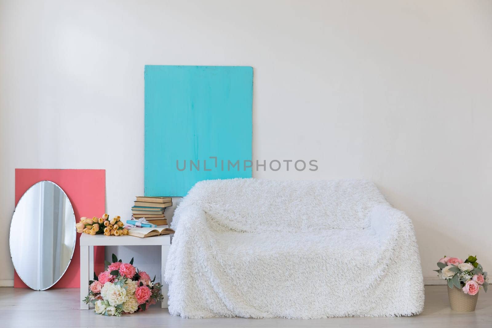 White sofa with flower vases in the interior of a white room with a window