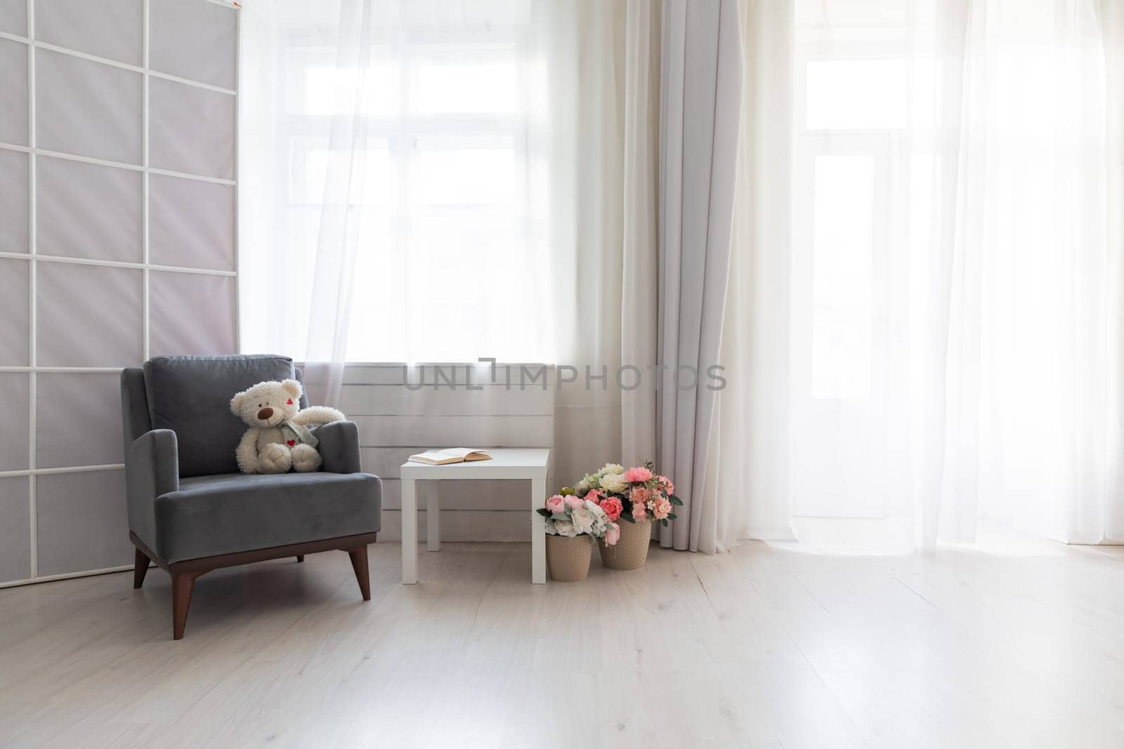 Armchair with toy book and flowers in the interior of a white room with a window