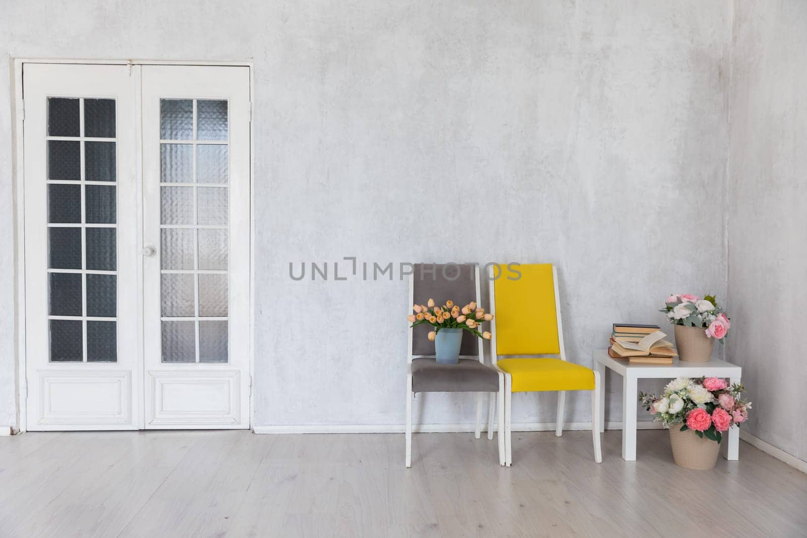 two chairs and a table with books and flowers in the interior of a white room