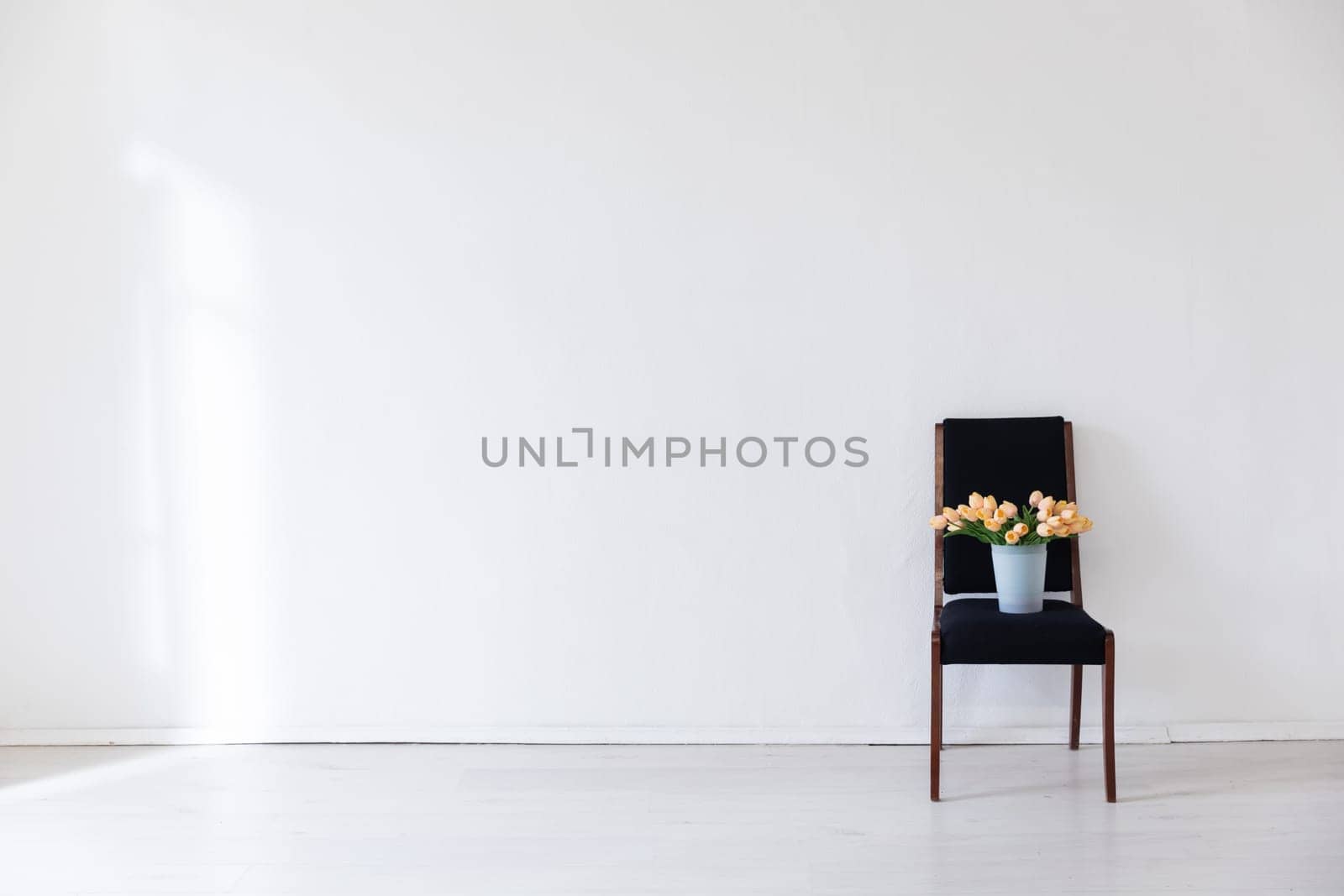 One black chair with flowers in the interior of a white room with a window