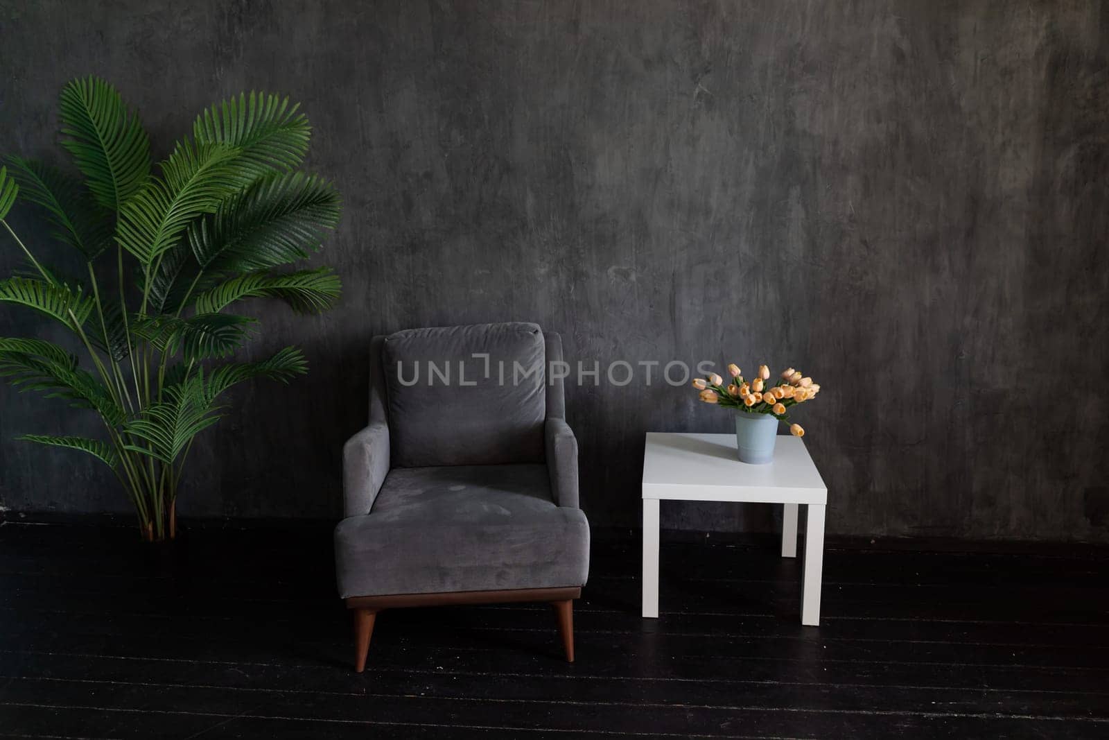 gray armchair and table with vase of flowers in dark room interior