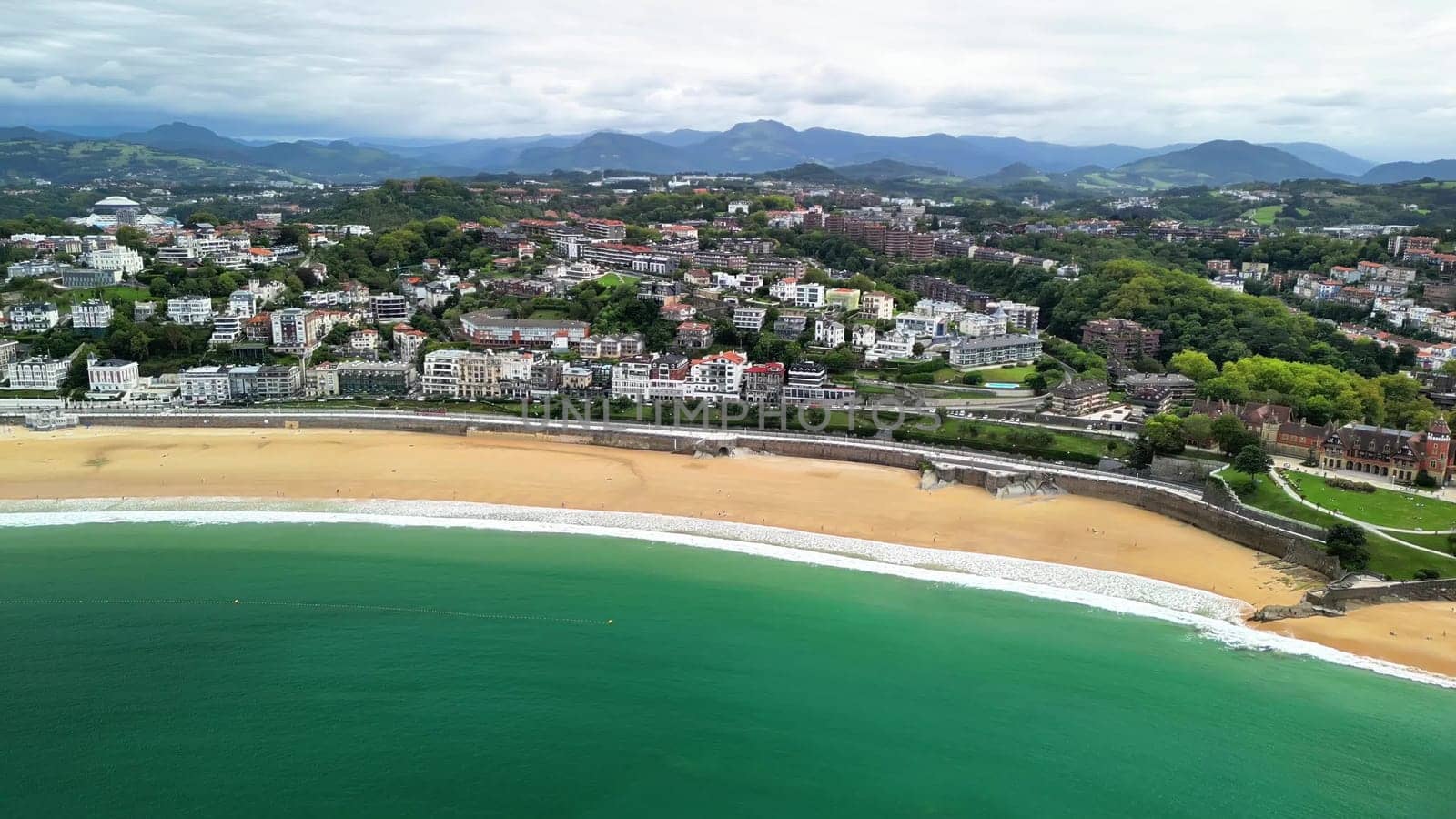 The aerial view showcases a beautiful beach and coastal town with vibrant blue waters and soft, sandy shores