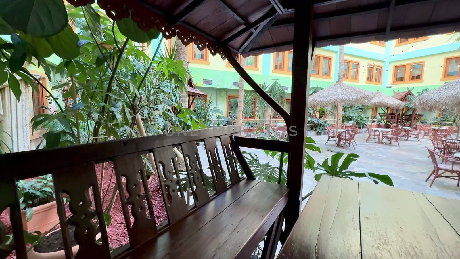 An inviting outdoor seating area features stylish wooden furniture amidst vibrant greenery at a charming restaurant
