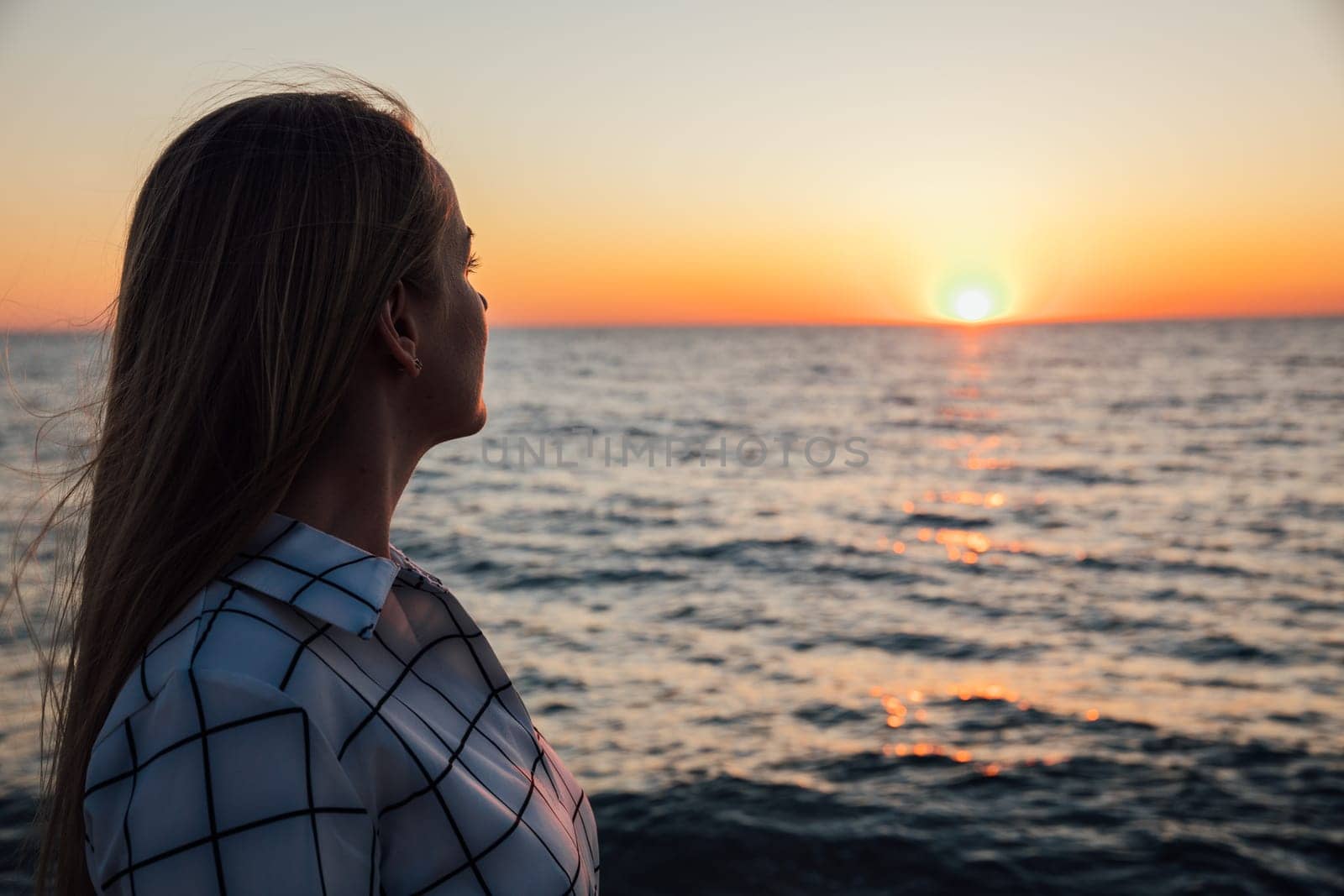 Blonde woman looking at sunset on the sea from the beach